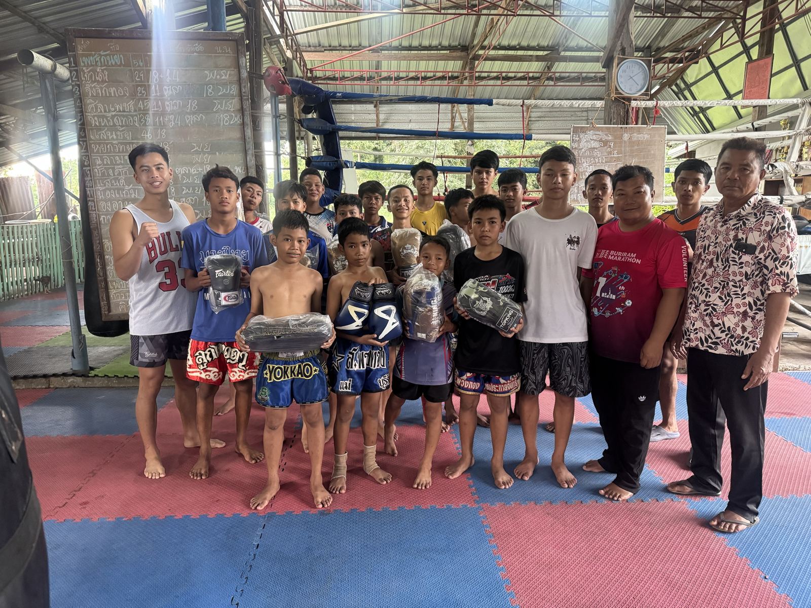 Kids from a village gym in Isan holding their new gloves and pads, with their trainers